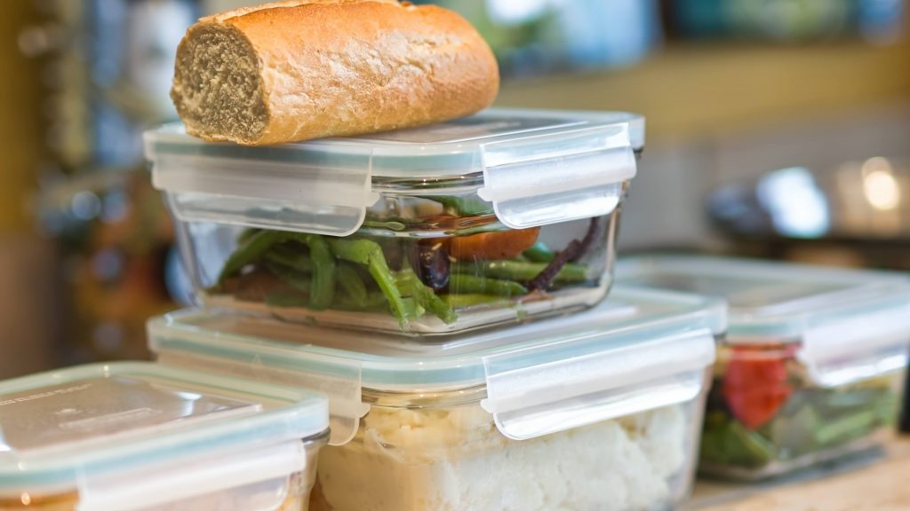 several plastic containers with leftover food, stacked on top of each other on a kitchen counter
