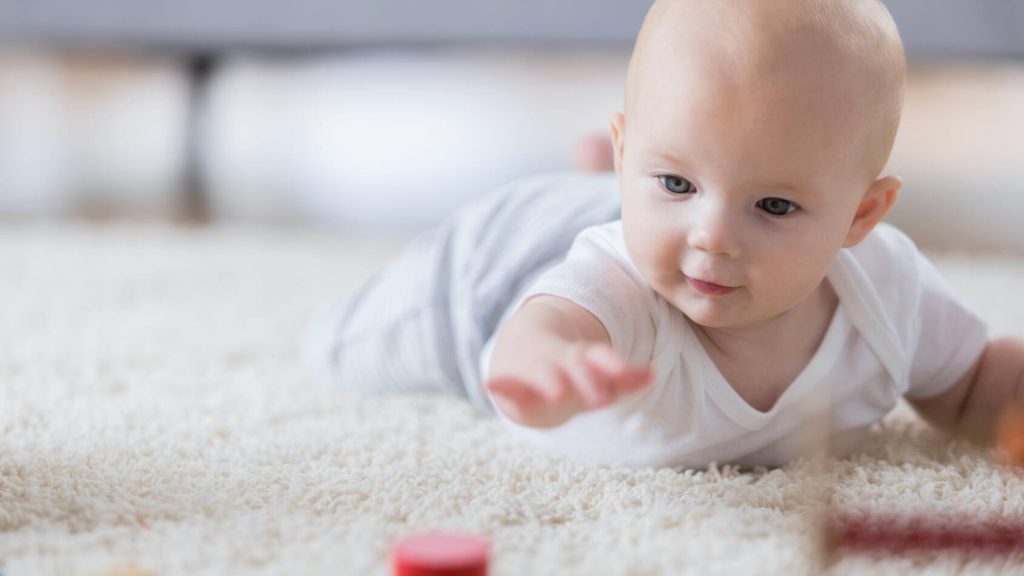 Baby, lying on stomach, reaching for blocks