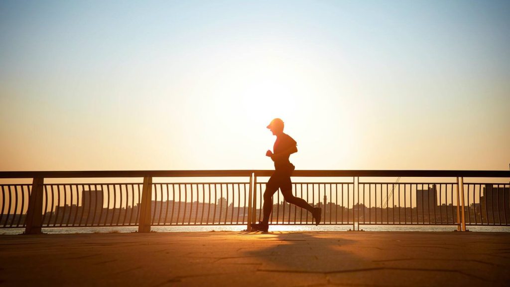 man running in the sun, wearing a hat for protection, crossing a bridge
