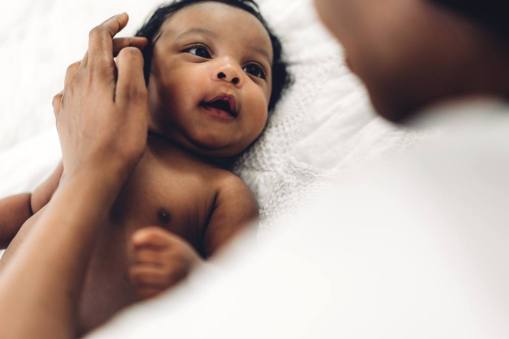 African american mother playing with adorable little african american baby in a white bedroom