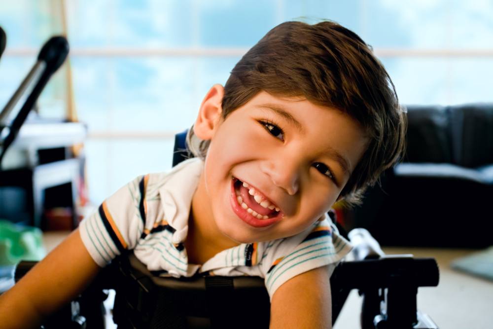 little boy with disability standing in walker smiling and happily looking at camera with bright blue sky and clouds in the background window