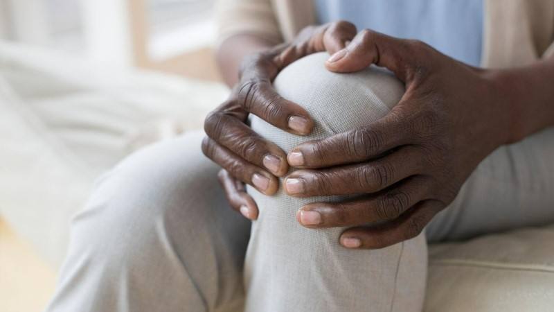 Black woman holding her knee in pain from an injury, osteoporosis, arthritis (which may lead to knee replacement surgery.)