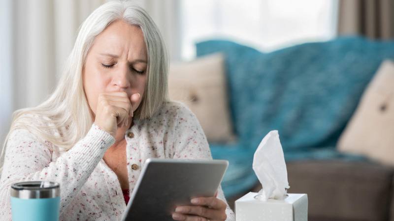 Middle-aged woman, coughing while looking at electronic tablet