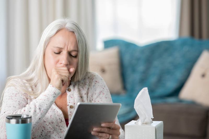 Middle-aged woman, coughing while looking at electronic tablet