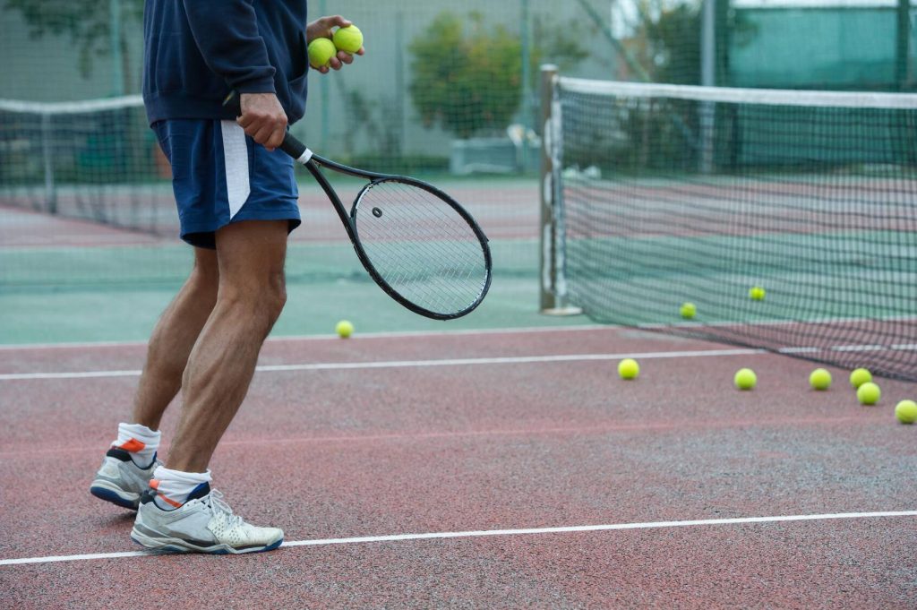 Cropped view of person on a tennis court with tennis balls and a racket in hand