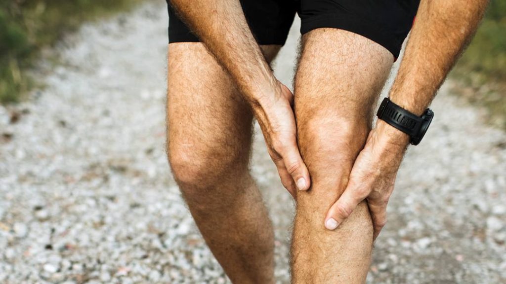 the legs and knees of a man in running shorts, holding his left knee with both hands