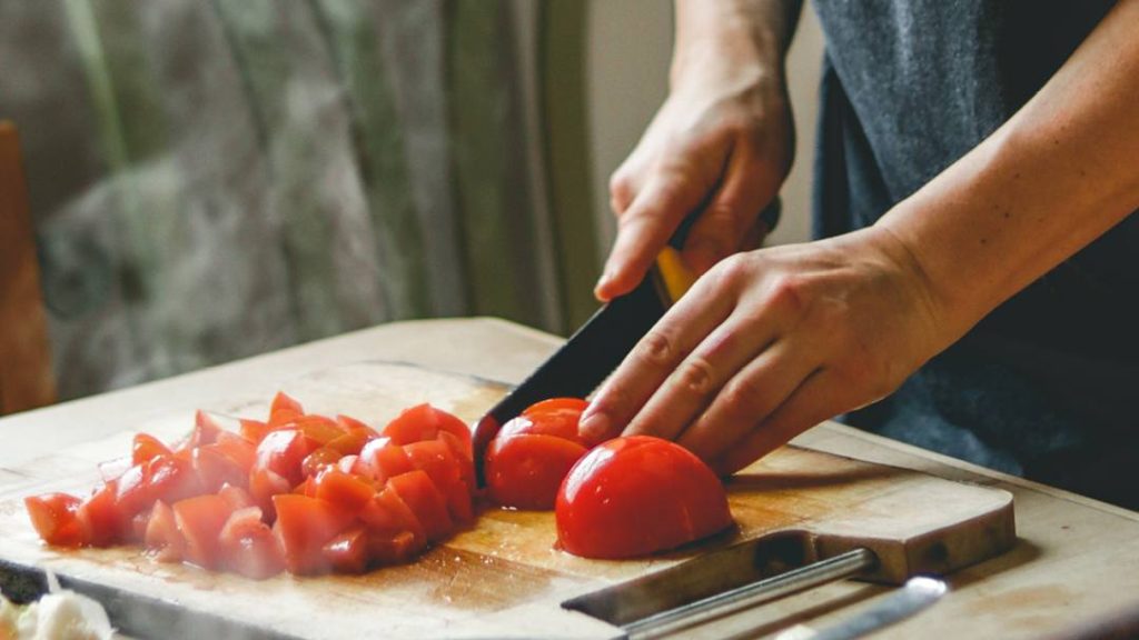 a close-up of a person's hands chopping tomatoes on a wooden cutting board