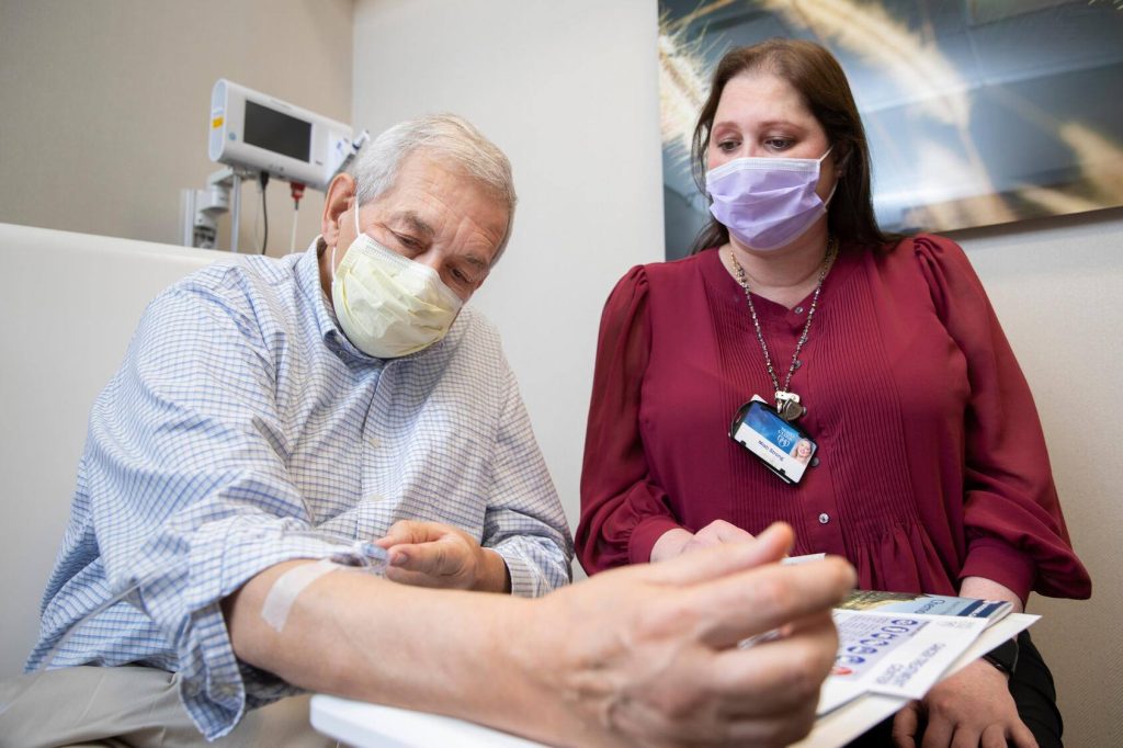Masked staff member shows literature to masked cancer patient receiving treatment