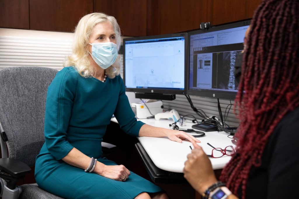 Physician wearing a mask in an exam room consulting with a patient
