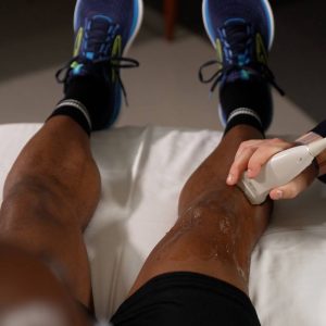 Physician using an ultrasound machine on a Black male's leg.