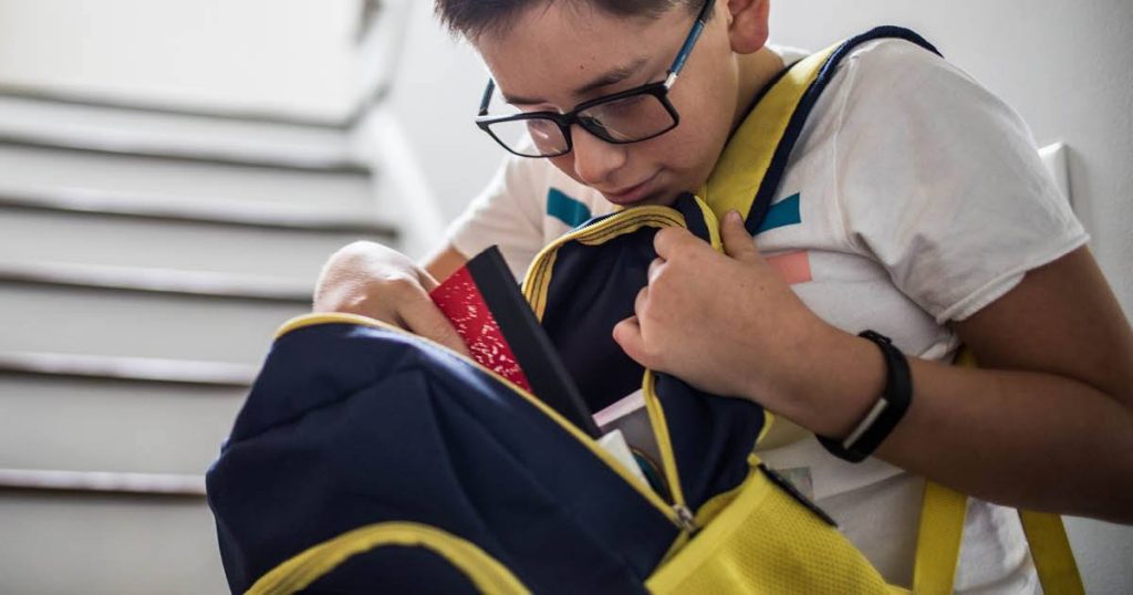 young male in glasses looking through his backpack