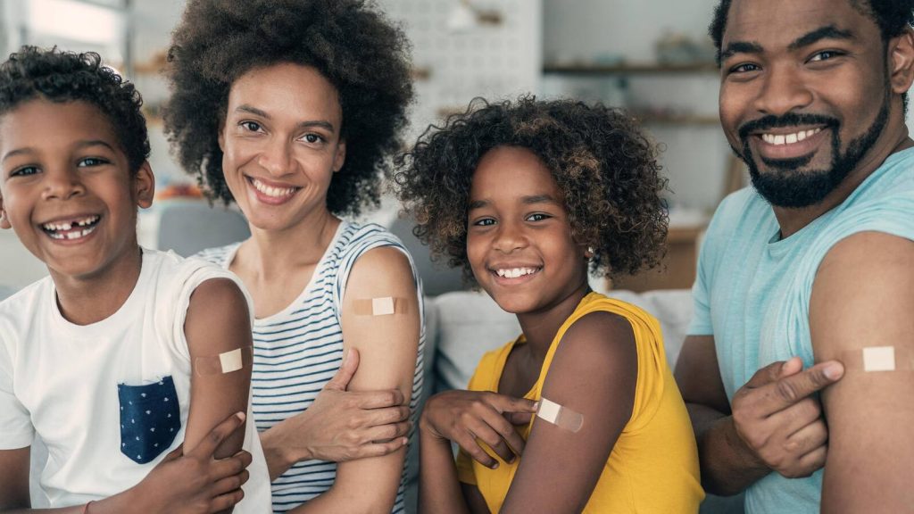 Family of four smiling and pointing at their bandages, indicating they just had their flu  shot