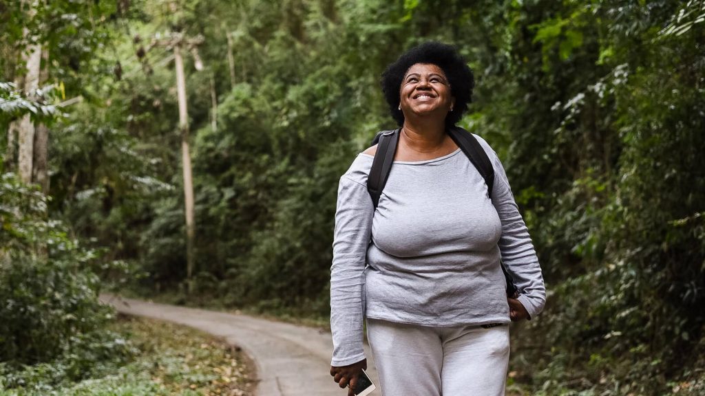 Happy, smiling woman walking with her phone while outdoors on path, Black/African American woman, outdoors, exercising, walk, exercise, hiking