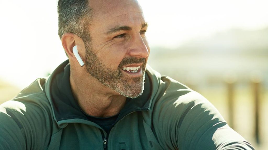 a smiling middle age white man outdoors on a sunny day, with a wireless earbud in one ear