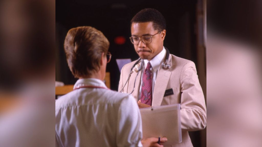 Dr. Floyd Willis, wearing a stethoscope, receives a diploma from an unidentified person at the 1989 Mayo Graduate School of Medicine commencement.