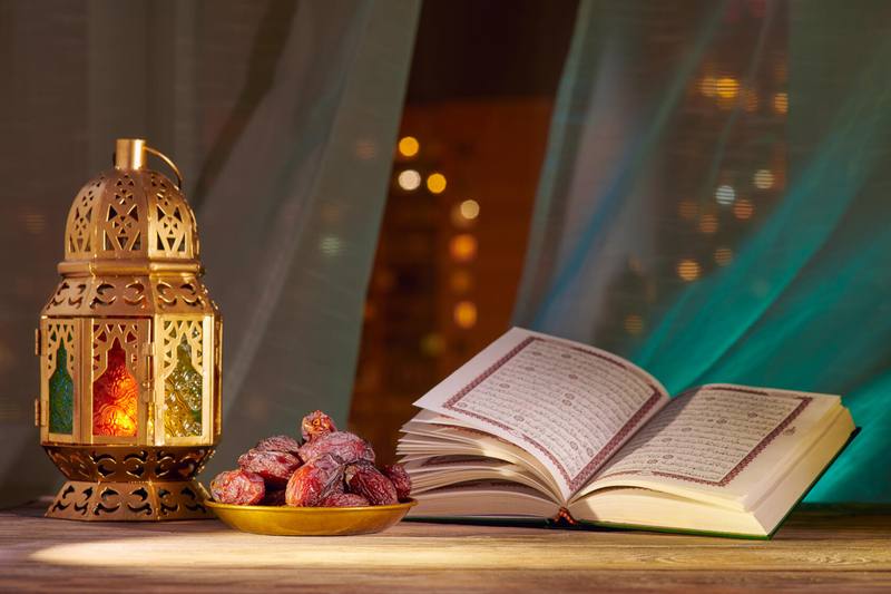 An open Quran rests next to a bowl of dates and a decorated lantern