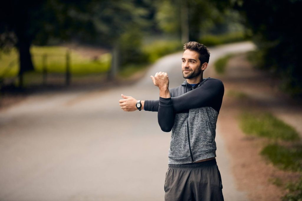 a young man outdoors, stretching his arms before a run