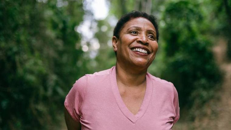 photograph of middle-aged Black woman in pink shirt, outside, smiling