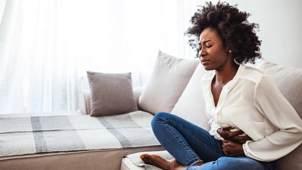 Young Black woman sits on sofa in pain