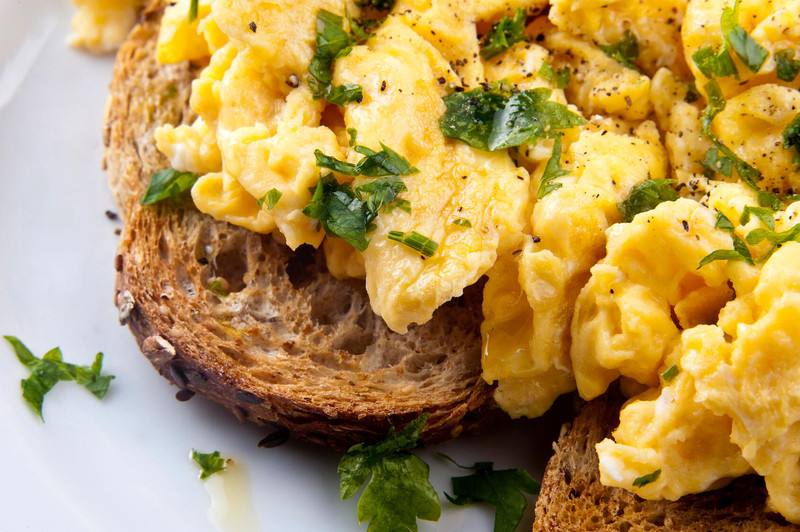 a close-up of scrambled eggs with herbs and seasonings on whole grain toast