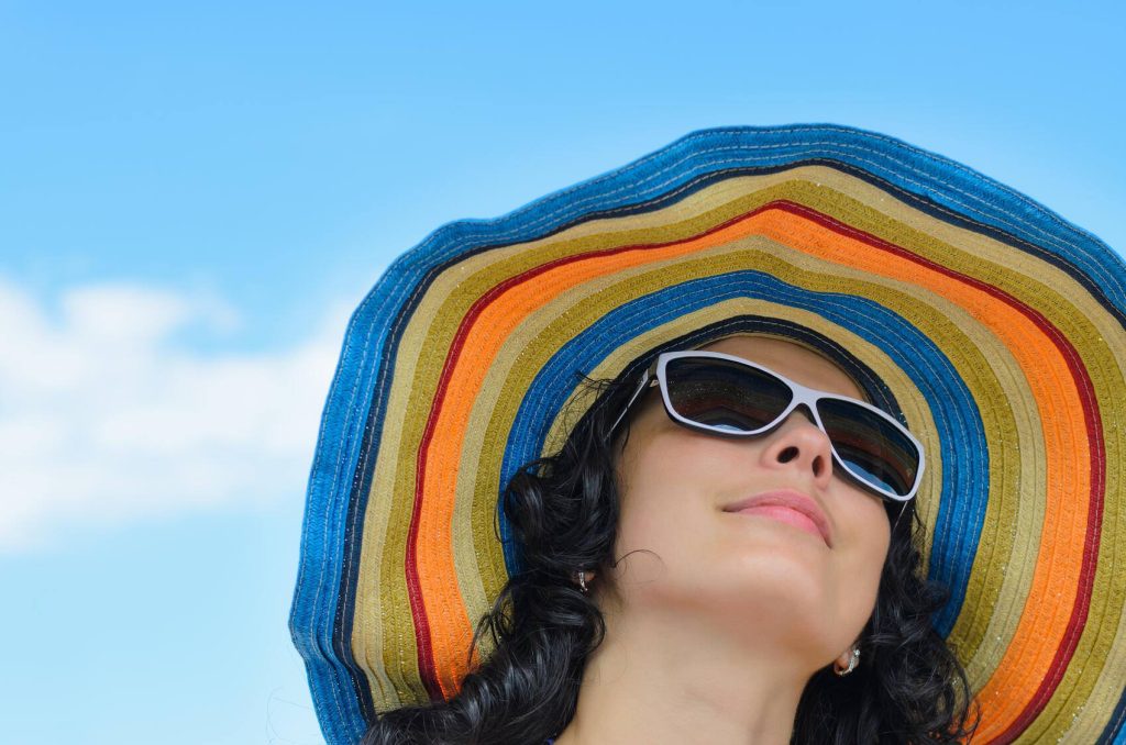 close-up of a young woman outdoors, wearing sunglasses and a colorful wide-brimmed hat - for sun safety.