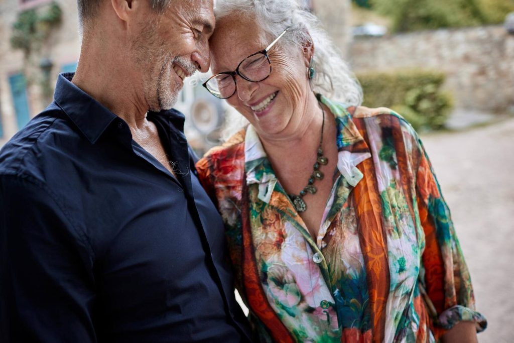 a happy older white couple outdoors, standing close together and laughing