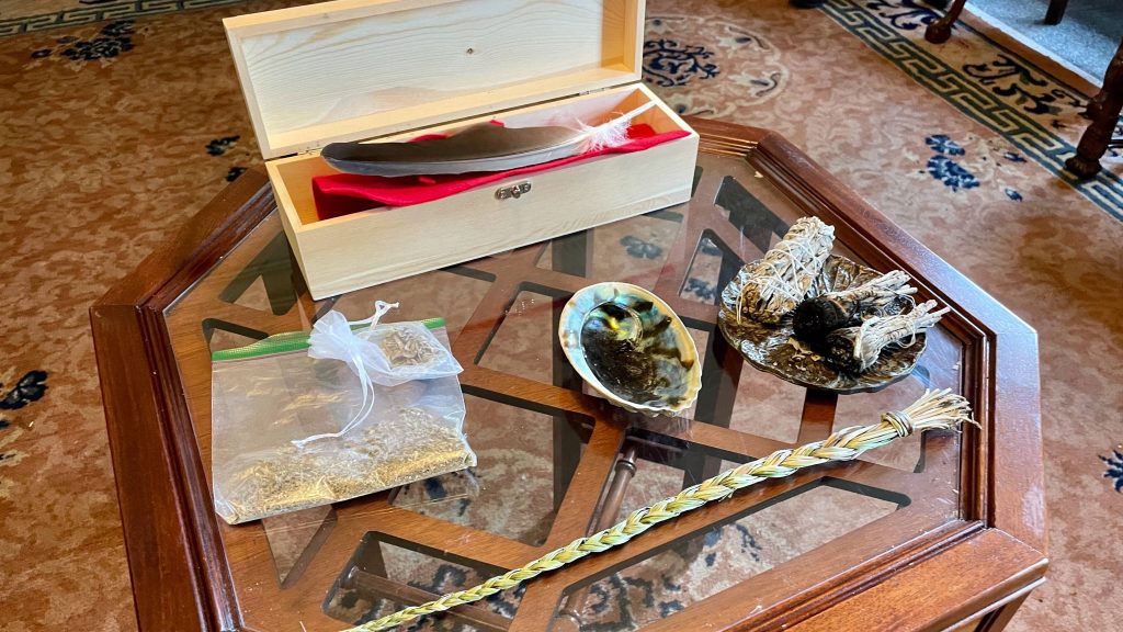 Photograph of smudging table from Saint Marys. Eagle feather, sweet grass, tobacco, Abalone shell.