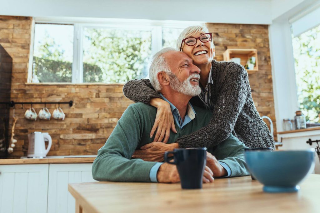 a happy older white man and woman smiling and embracing in the kitchen