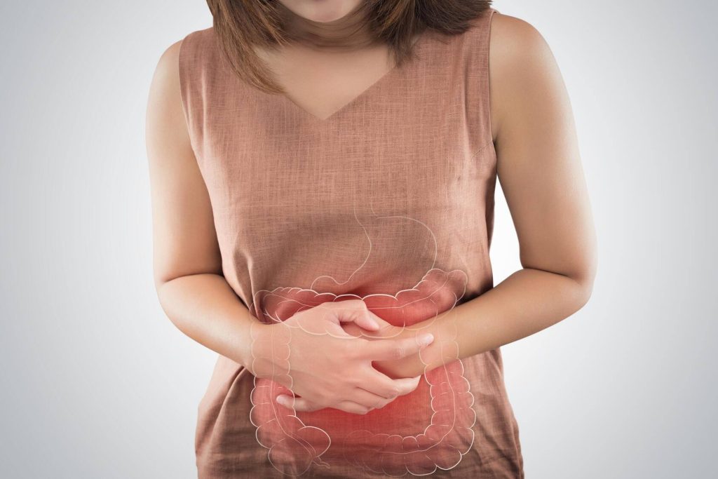 a young white woman holding her belly as though she's in pain, with a graphic of her stomach and intestines overlaid and highlighted in red