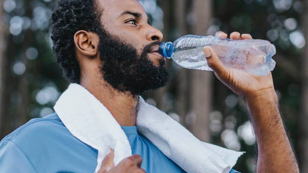 Photograph of young man with beard, towel around his neck, drinking bottle of water
