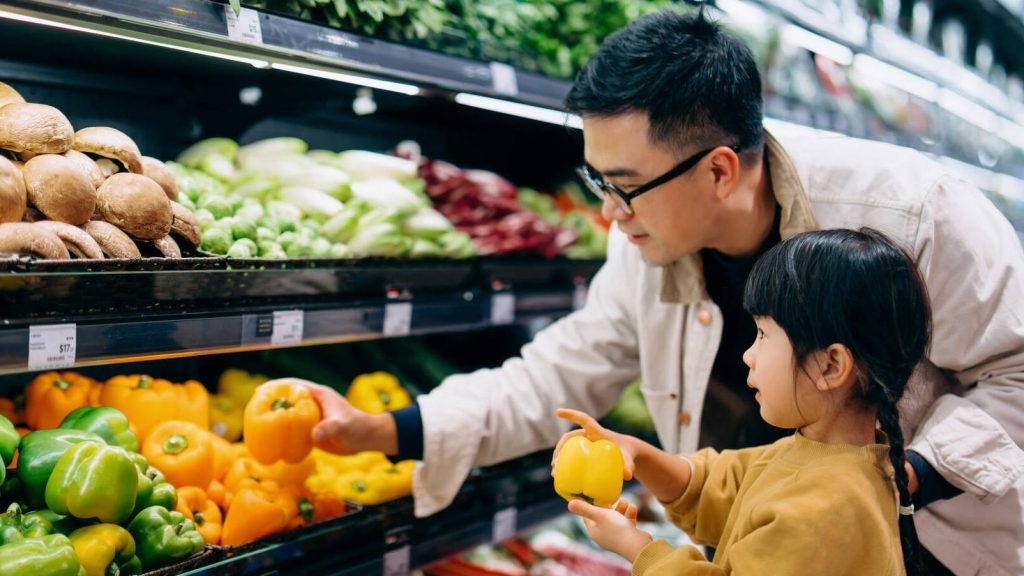 Man with young child picking out fresh vegetables produce at grocery