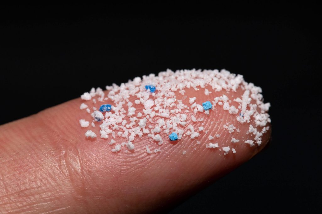 A close-up view of white and blue microplastic pieces on a fingertip.