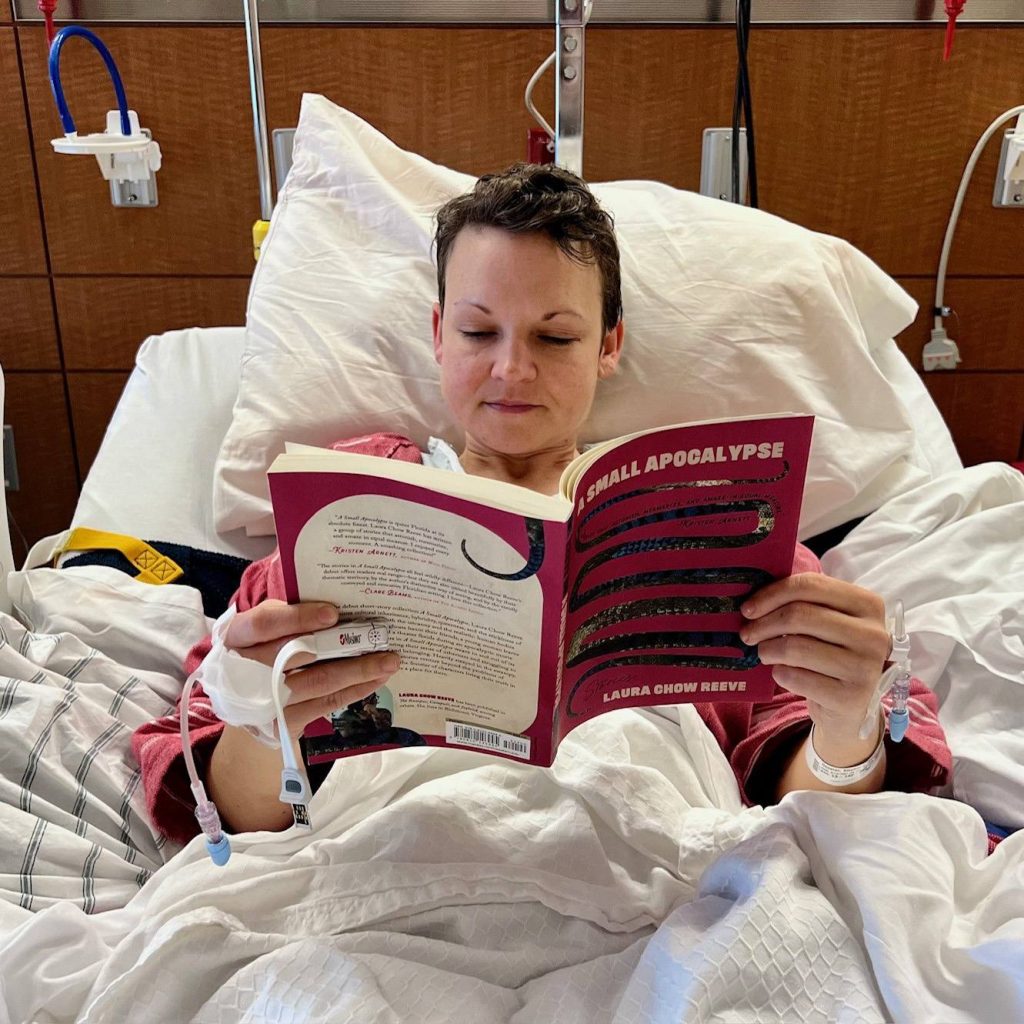 Stephanie Donelan sitting up in a hospital bed reading a book..