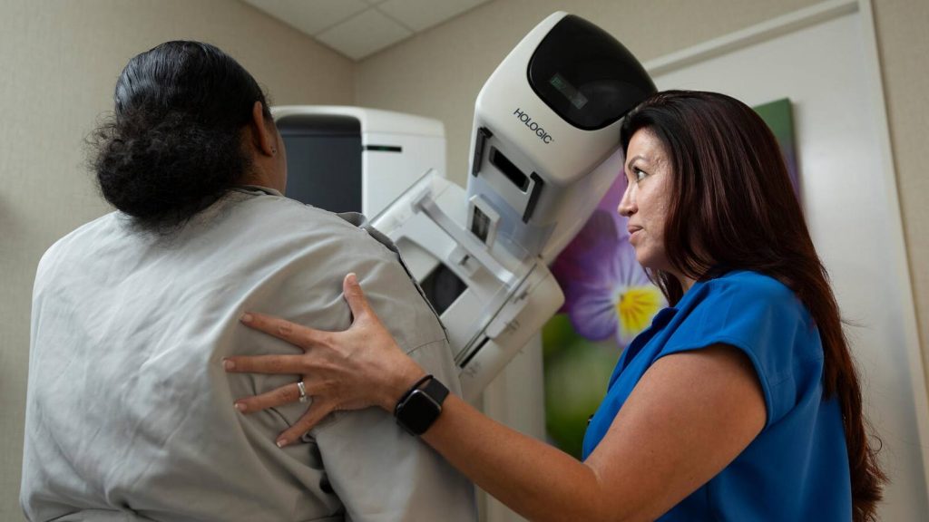 An ultrasound technician positions a patient for a mammogram, a breast cancer screening tool