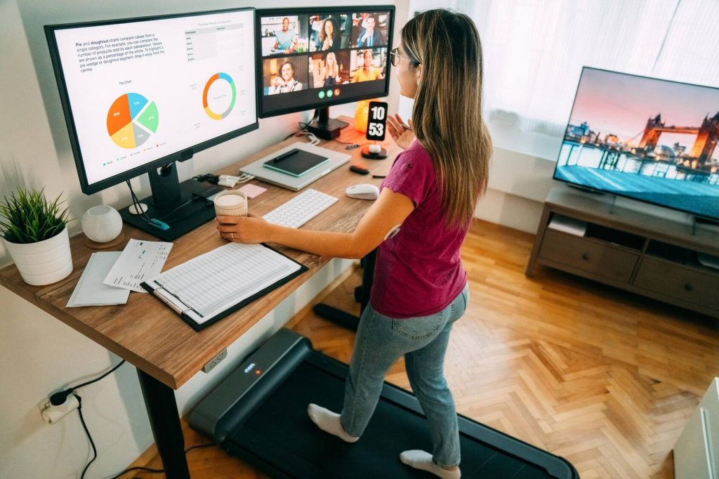 A woman working from home uses an under the desk treadmill at her standing desk