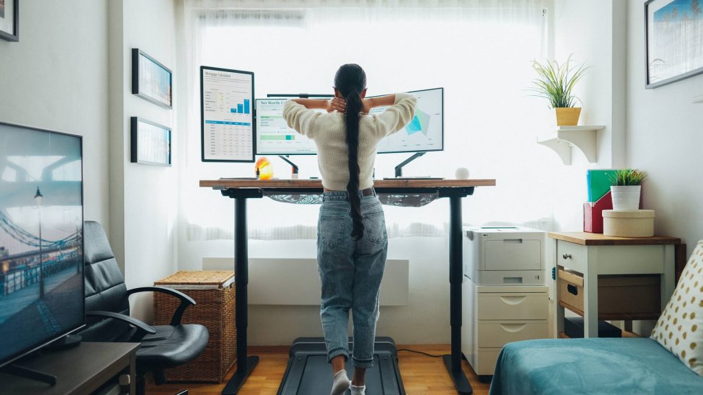 back of woman rubbing neck while walking on treadmill at desk, active workstation