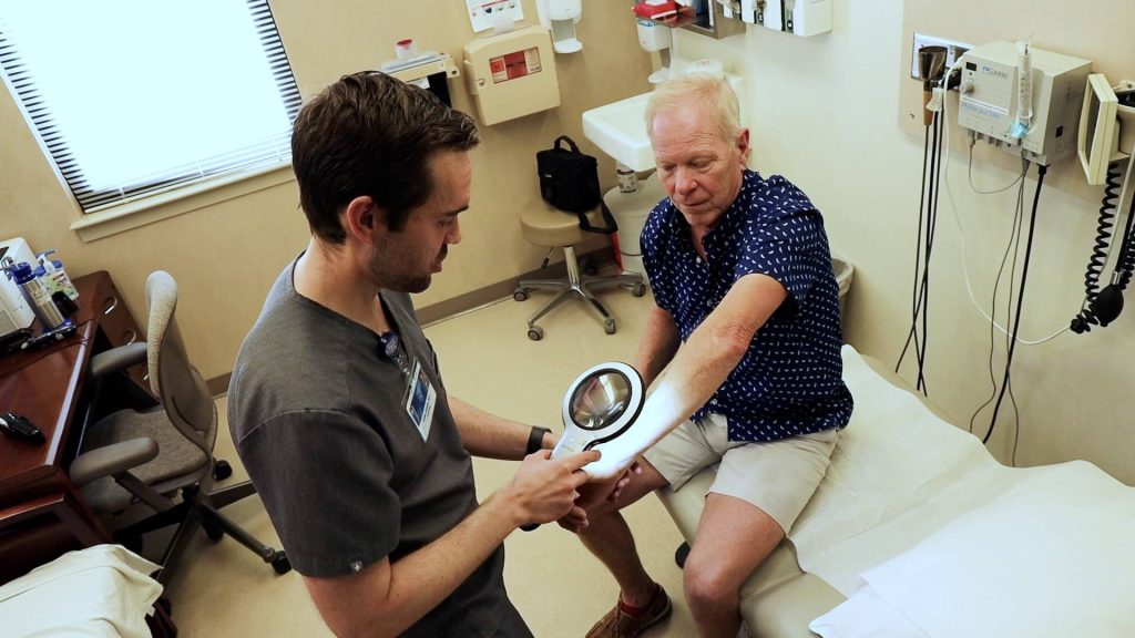 Dr. Collin Costello checking man for skin cancer