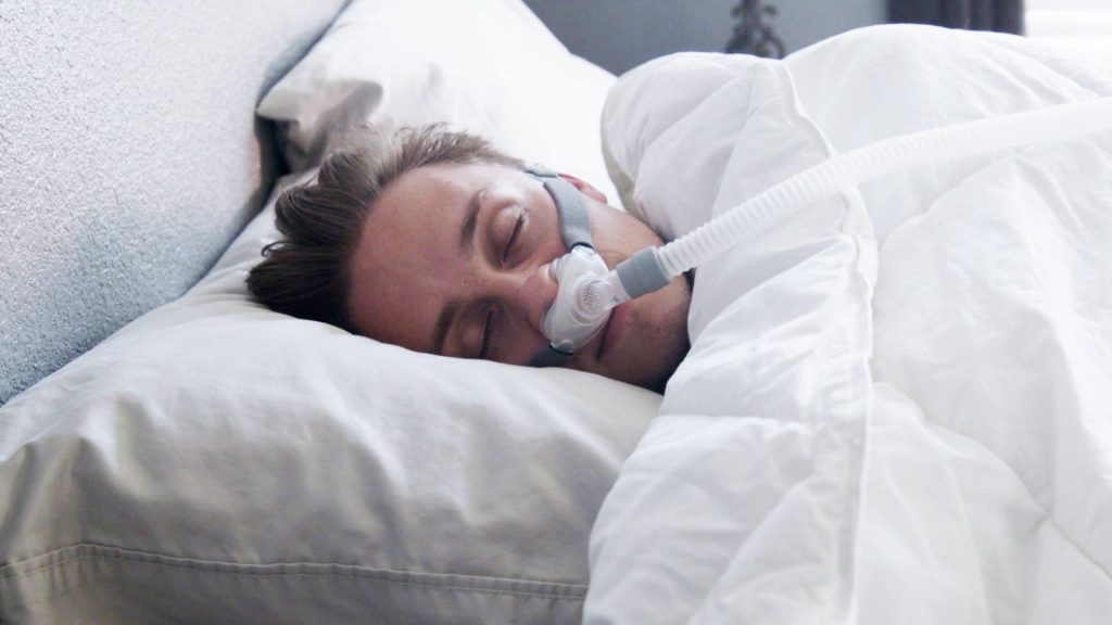 A man is sleeping in bed with a CPAP machine.