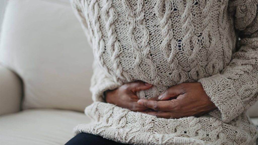 Close-up of unrecognizable Black woman sitting on sofa holding her abdomen in pain. Getty Images