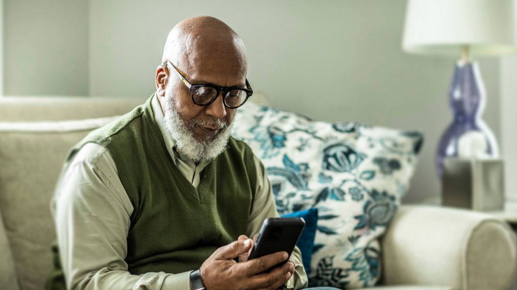 Older, middle aged man, beard, Black male sitting on couch, looking at mobile phone