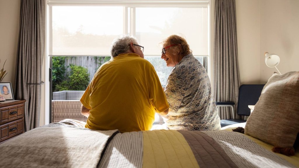 man, woman, older couple, sits on bed facing window