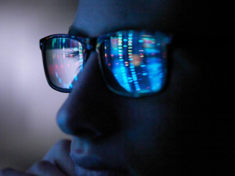 Deoxyribonucleic acid (DNA) profile graphics are reflected from a computer screen into a person's eyeglasses, in a dark room