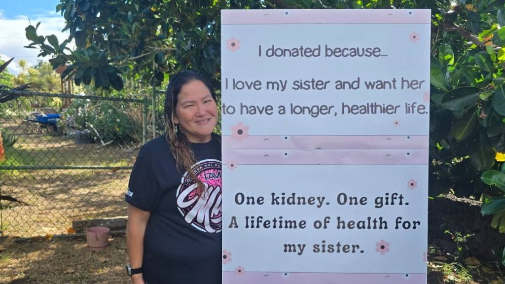 Charnel Golis-Tabag stands with sign showing why she donated a kidney, Charnel donated a kidney to her sister.
