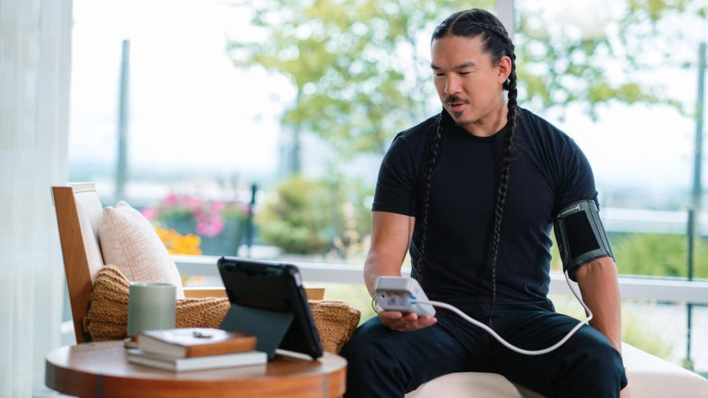 Young male patient takes his own blood pressure reading during a virtual telehealth visit.
