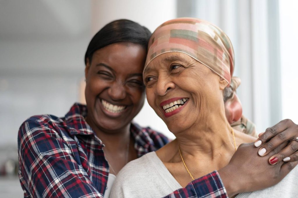 A woman hugs her mother as they both smile. The mother is wearing a headscarf indicating cancer treatment.
