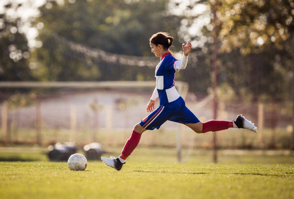 Young woman, teen, kicks a soccer ball, ACL injuries are more common in females than males