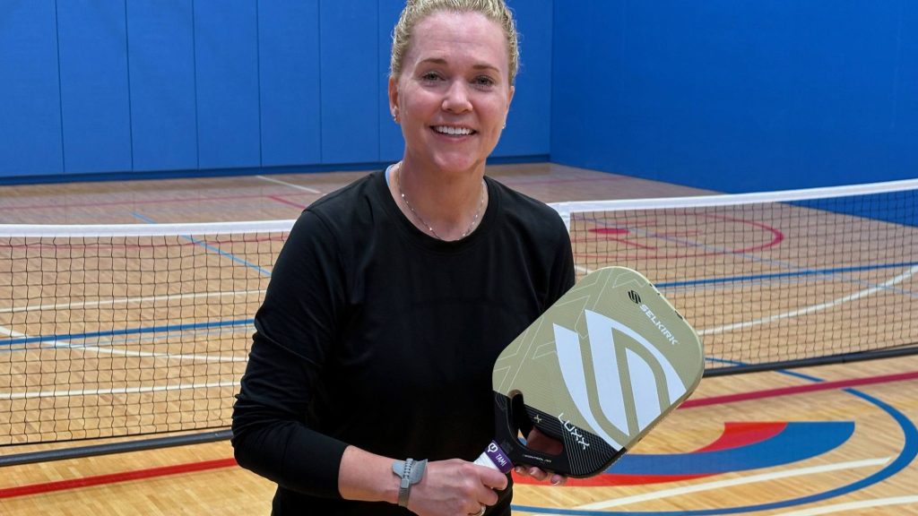 Tami Lucius holding a pickleball paddle on a pickleball court. She had innovative wrist surgery at Mayo Clinic.