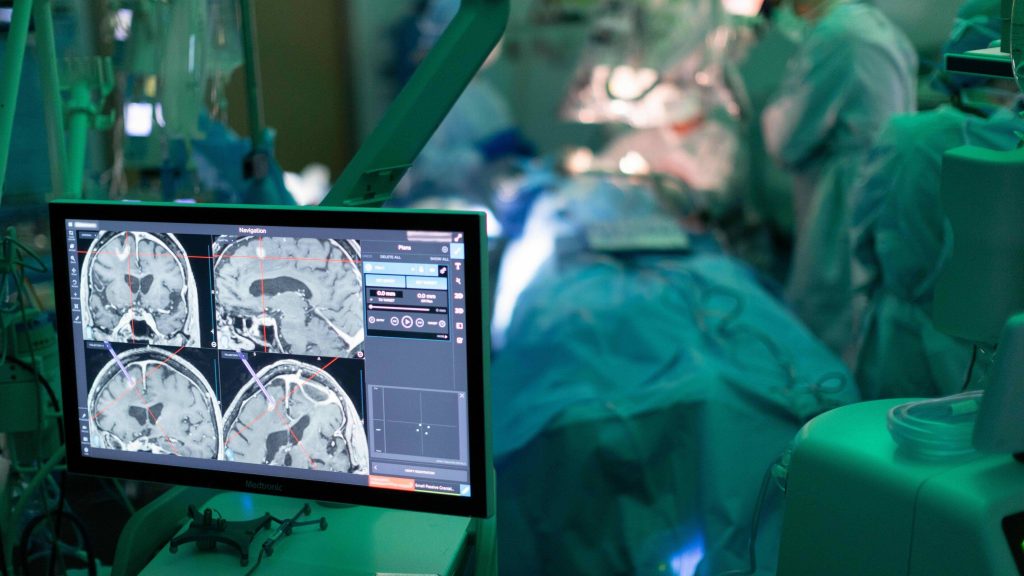 Neurosurgeon using surgical navigation system with cranial images displayed in the foreground, brain tumor treatment
