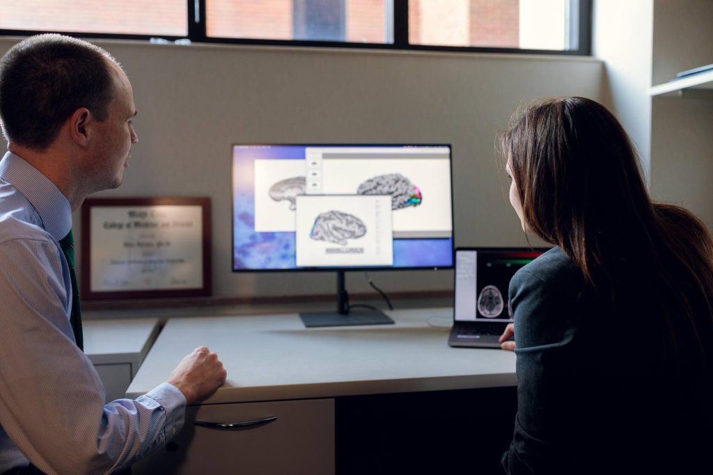 Dr. Nick Gregg, neurologist, and Dr. Dora Hermes Miller, biomedical engineer, look at brain imaging on a computer in the Multimodal Neuroimaging lab.