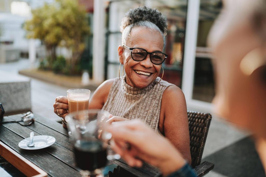 Two senior friends drink coffee at an outdoor café.